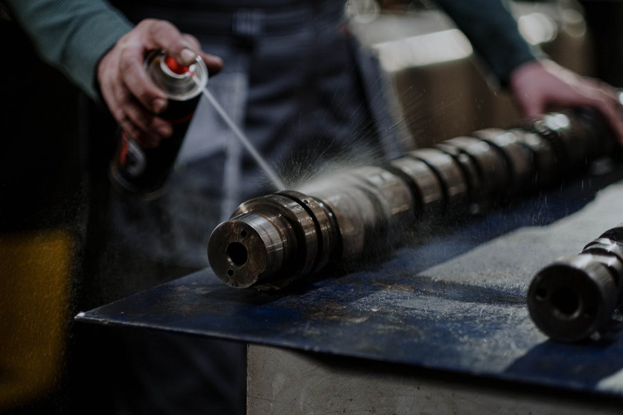 Mechanic meticulously sprays degreaser onto an engine camshaft for maintenance.